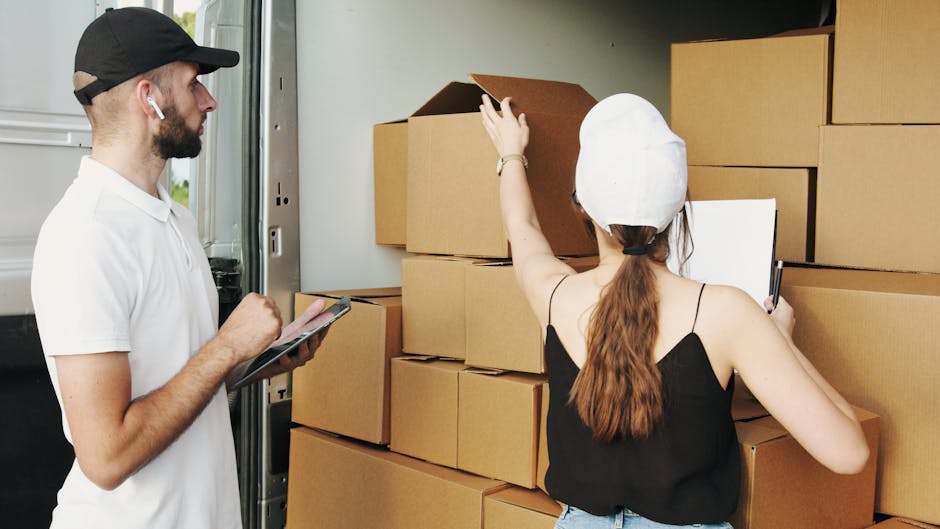 Inside a van used for home relocation, several medium-sized cardboard boxes are stacked near the open side door. The boxes are sealed with packing tape and vary slightly in size, indicating they are p
